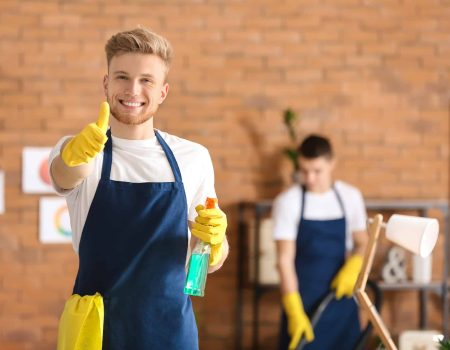 Male janitor showing thumb-up gesture in office during cleaning